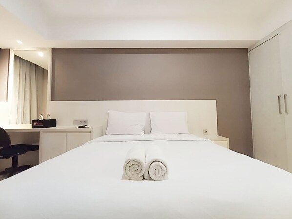 Una camera d'albergo con un letto rifatto, una scrivania con una sedia e un armadio.