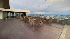 A rooftop terrace with wicker furniture and string lights, overlooking a cityscape. - Good Choice And Modern Studio Marquis De Lafayette Apartment (Semarang)