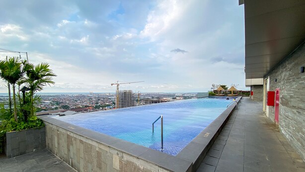A rooftop infinity pool with a city view, surrounded by a stone deck and a modern building. - Good Choice And Modern Studio Marquis De Lafayette Apartment (Semarang)