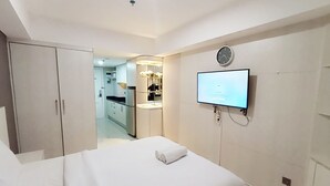 A modern hotel room with a bed, a TV mounted on the wall, a small kitchenette, and a bathroom visible through an open door. - Good Choice And Modern Studio Marquis De Lafayette Apartment (Semarang)