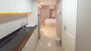 A narrow hotel corridor with a kitchenette on the left, a bed in the middle, and a door on the right. - Good Choice And Modern Studio Marquis De Lafayette Apartment (Semarang)