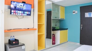 A hotel room with a TV mounted on the wall, a minibar, a sink, and a door. - Comfy Studio Apartment At Jarrdin Cihampelas (Bandung)