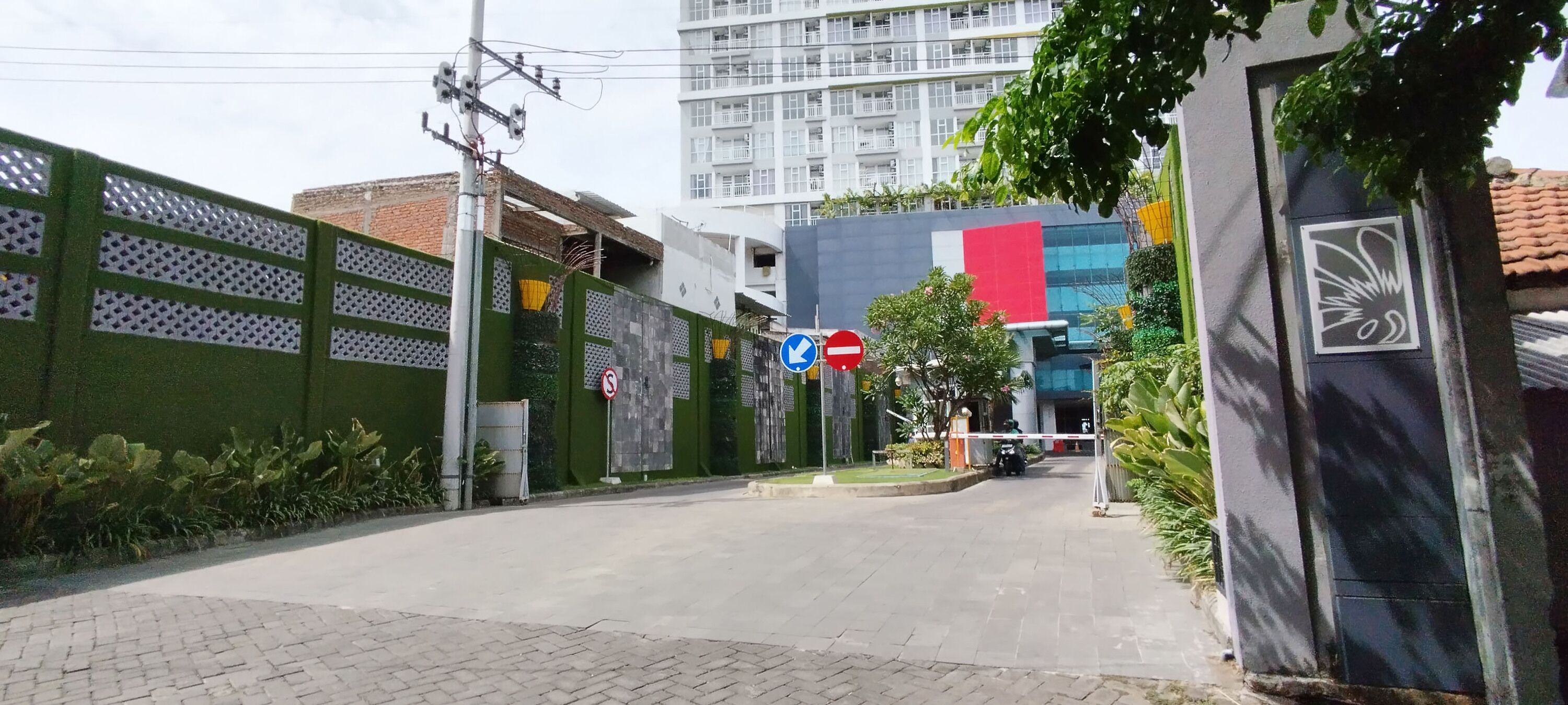A gated entrance with a no-entry sign, a blue directional arrow sign, and a building with a modern facade in the background.