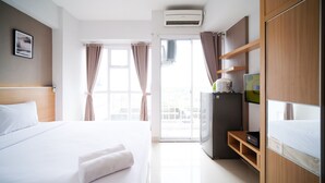 Habitación de hotel con cama, escritorio, refrigerador y ventana con cortinas.