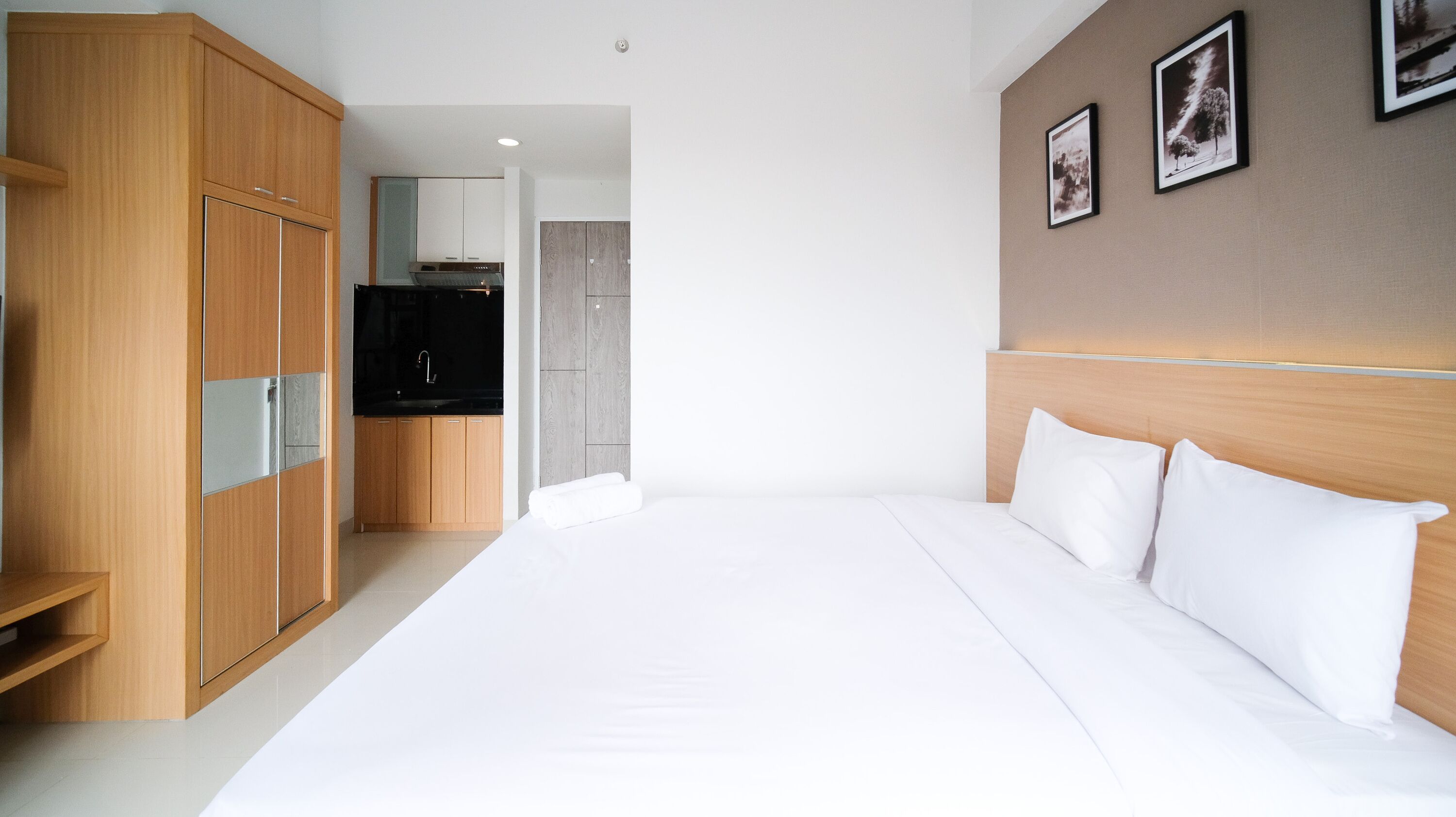 A hotel room with a large bed, wooden wardrobe, and a kitchenette.