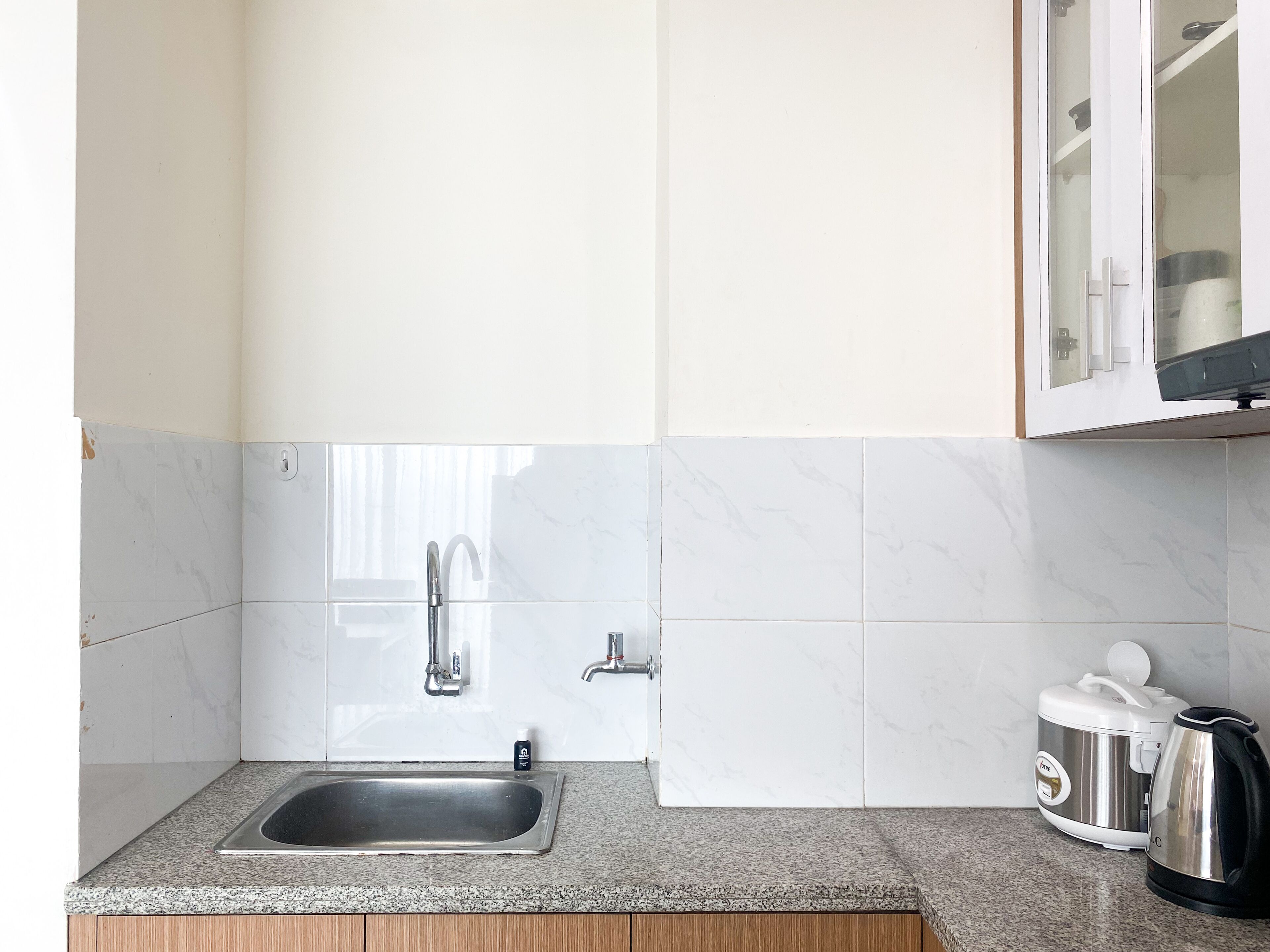 A kitchen with a stainless steel sink, a coffee maker, and a cabinet with a glass door.