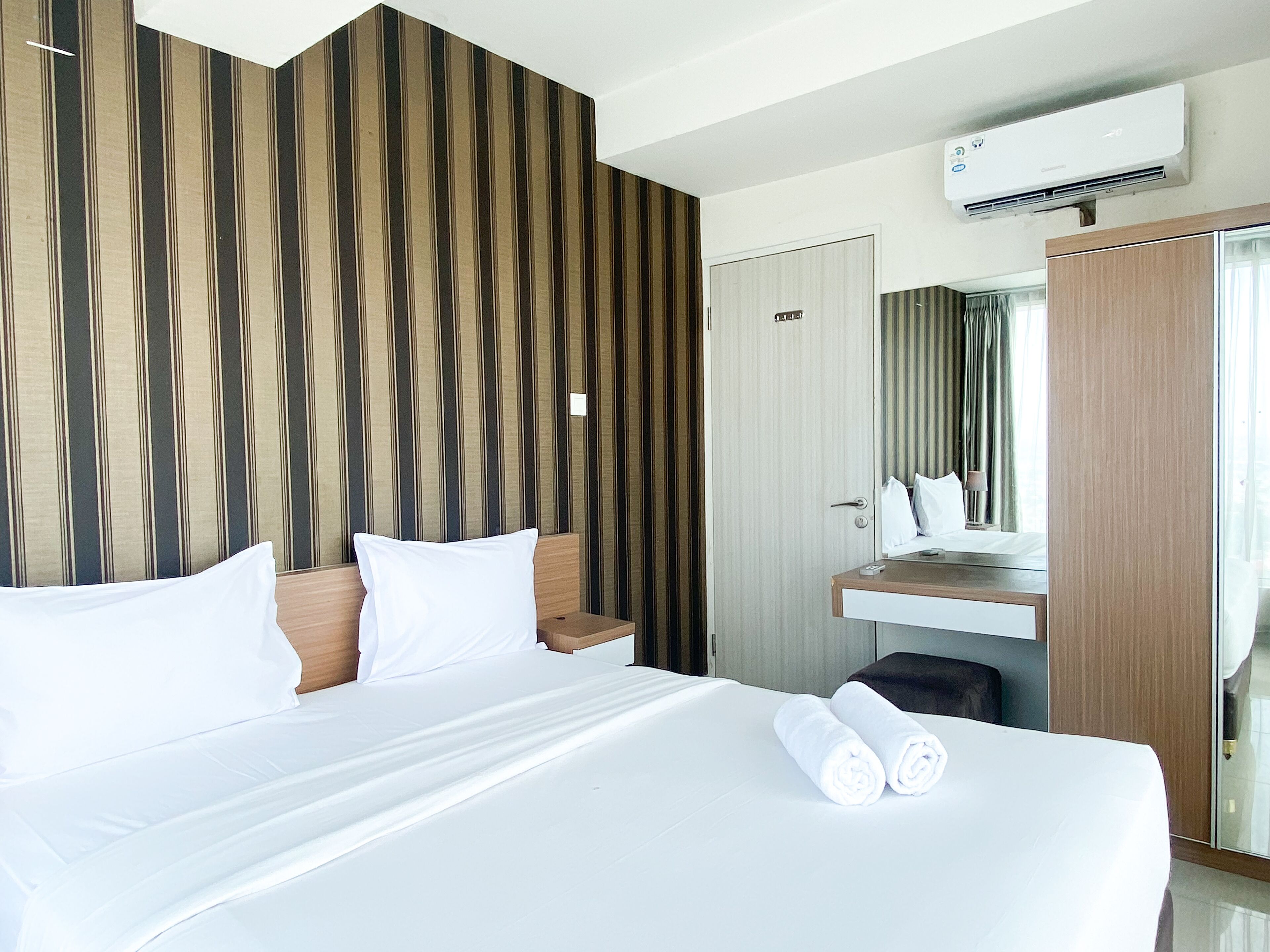 A hotel room with a large bed, a wooden headboard, a built-in desk, and a mirror above the desk.