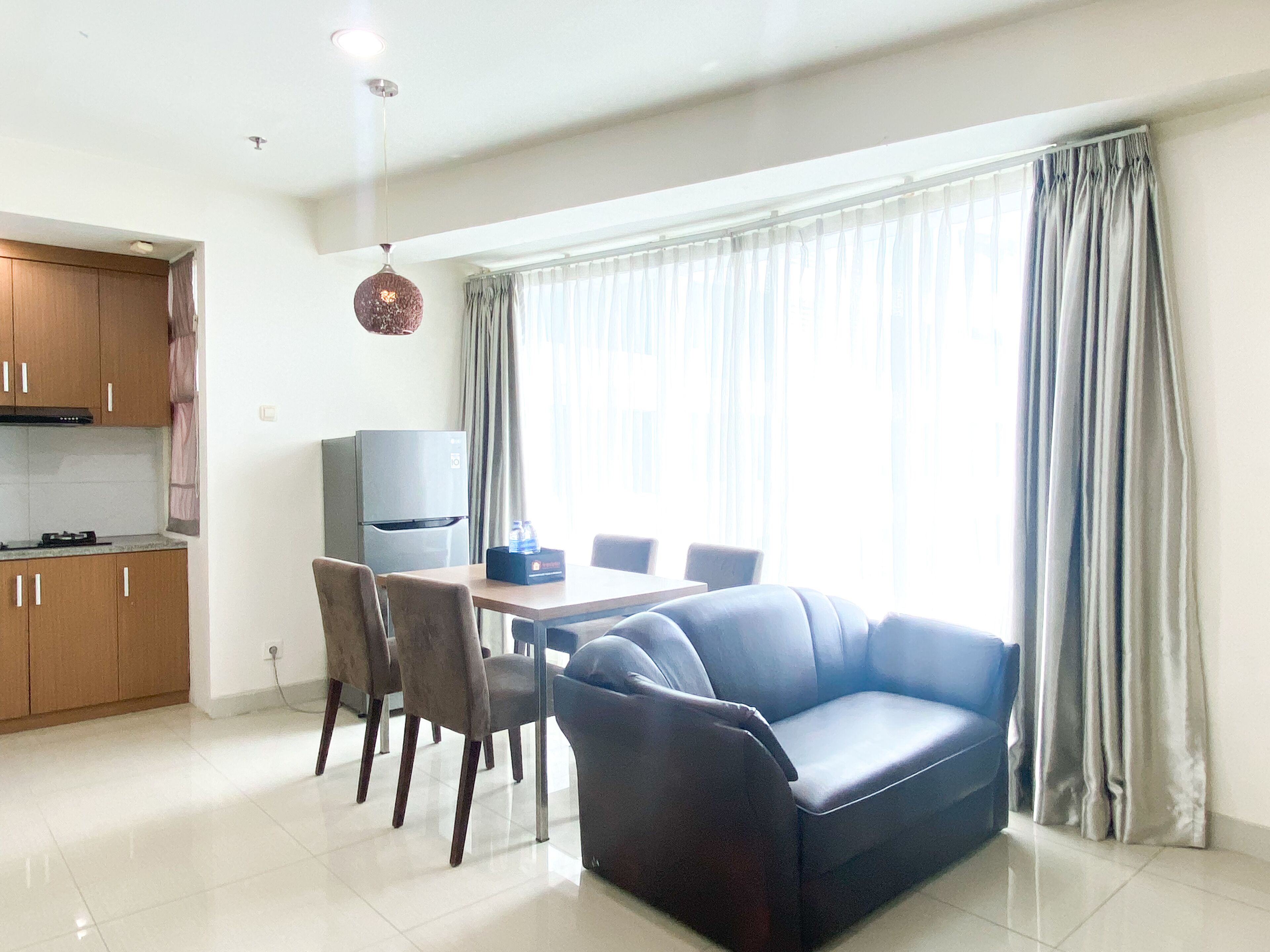 Una sala de estar moderna con sofá, mesa de comedor, sillas y una zona de cocina con armarios y un refrigerador.