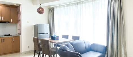 Una sala de estar moderna con sofá, mesa de comedor, sillas y una zona de cocina con armarios y un refrigerador.