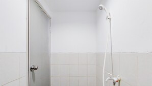 A bathroom with white tiled walls, a shower with a handheld showerhead, and a door with a silver handle. - Modern Look Studio At Urbantown Serpong Apartment (South Tangerang)