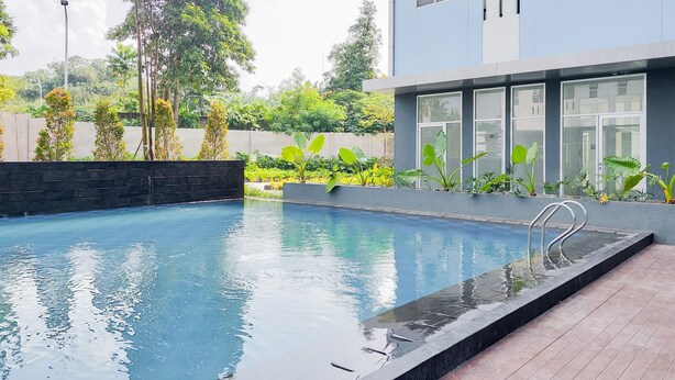 A modern building with a swimming pool, surrounded by lush greenery and a stone wall. - Modern Look Studio At Urbantown Serpong Apartment (South Tangerang)
