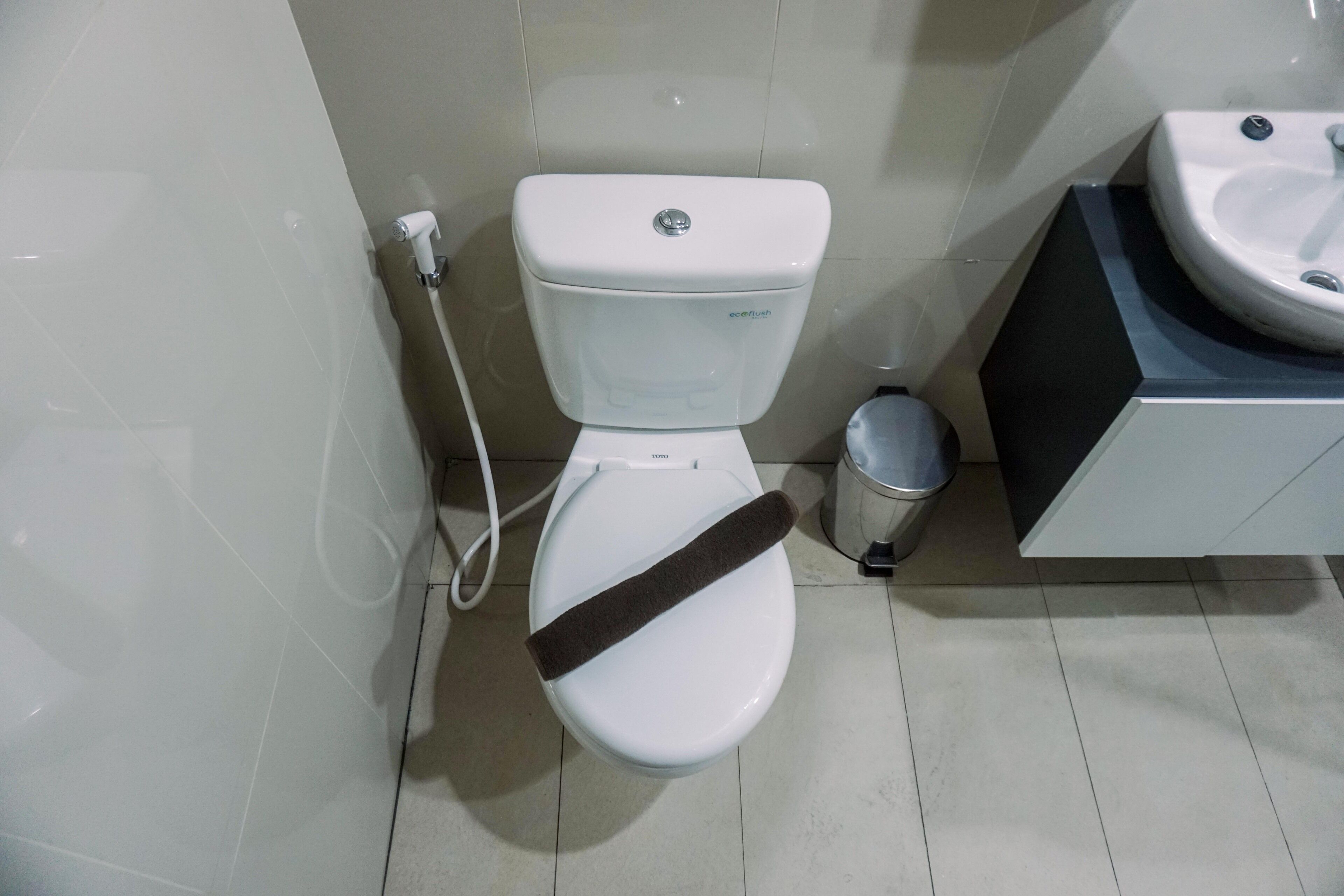 A toilet with a bidet attachment, a trash bin, and a sink.
