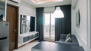 A modern living room with a sofa, a coffee table, and a TV unit. There is a balcony with a view of the city.