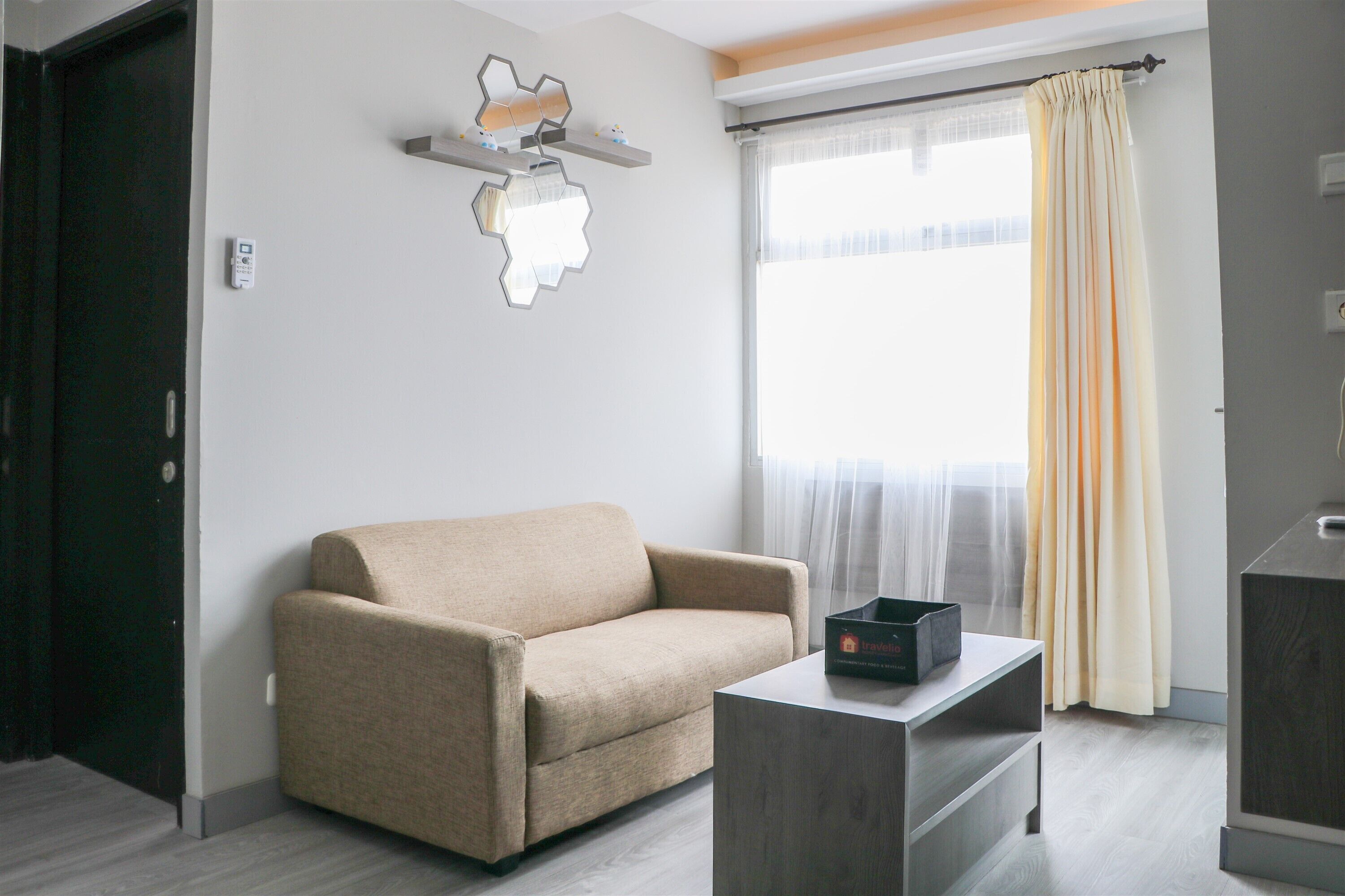 A modern living room with a beige sofa, a small coffee table, and a window with sheer curtains.