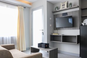A modern living room with a sofa, a coffee table, a flat-screen TV mounted on the wall, and a door with a curtain. - Brand New 2Br Apartment At Grand Asia Afrika (Bandung)