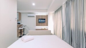 A hotel room with a bed, a TV mounted on the wall, a desk with a chair, and a window with curtains. - Relaxing Studio At Daan Mogot City Apartment (Jakarta)