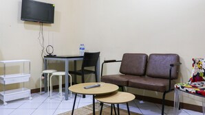 A small room with a flat-screen TV mounted on the wall, a brown sofa, two white chairs, a small round table, and a white shelf unit. - Best Deal 2Br At Buah Batu Park Apartment (Bandung)