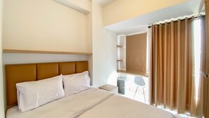 A hotel room with a large bed, a wooden headboard, a bedside table, and a window with curtains. - Relaxing And Cozy Studio Tokyo Riverside Pik 2 Apartment (Teluknaga)