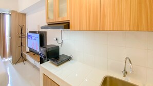 A modern kitchen with white tiles, wooden cabinets, a stainless steel sink, and a digital scale on the counter. - Relaxing And Cozy Studio Tokyo Riverside Pik 2 Apartment (Teluknaga)