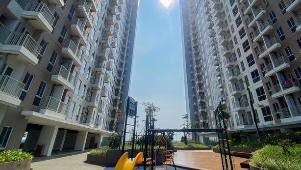 A high-rise residential building with multiple balconies, a central courtyard with exercise equipment, and a clear view of the sky. - Relaxing And Cozy Studio Tokyo Riverside Pik 2 Apartment (Teluknaga)