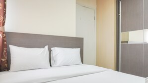 Une chambre d’hôtel avec un lit, du linge de lit blanc, une tête de lit en bois et une porte.
