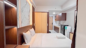 Hotelkamer met een bed, houten hoofdeinde, marmeren wand en een kitchenette met een koelkast en wastafel.