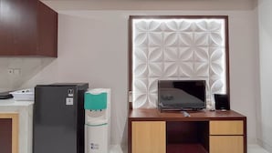 Een kleine keuken met een koelkast, een waterdispenser en een houten tafel met een laptop.