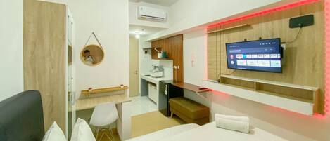 A modern hotel room with a bed, a desk, a chair, a TV, and a small kitchenette.