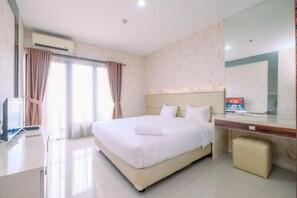 Quarto de hotel com uma cama grande, uma escrivaninha, uma cadeira, uma televisão e um banheiro.