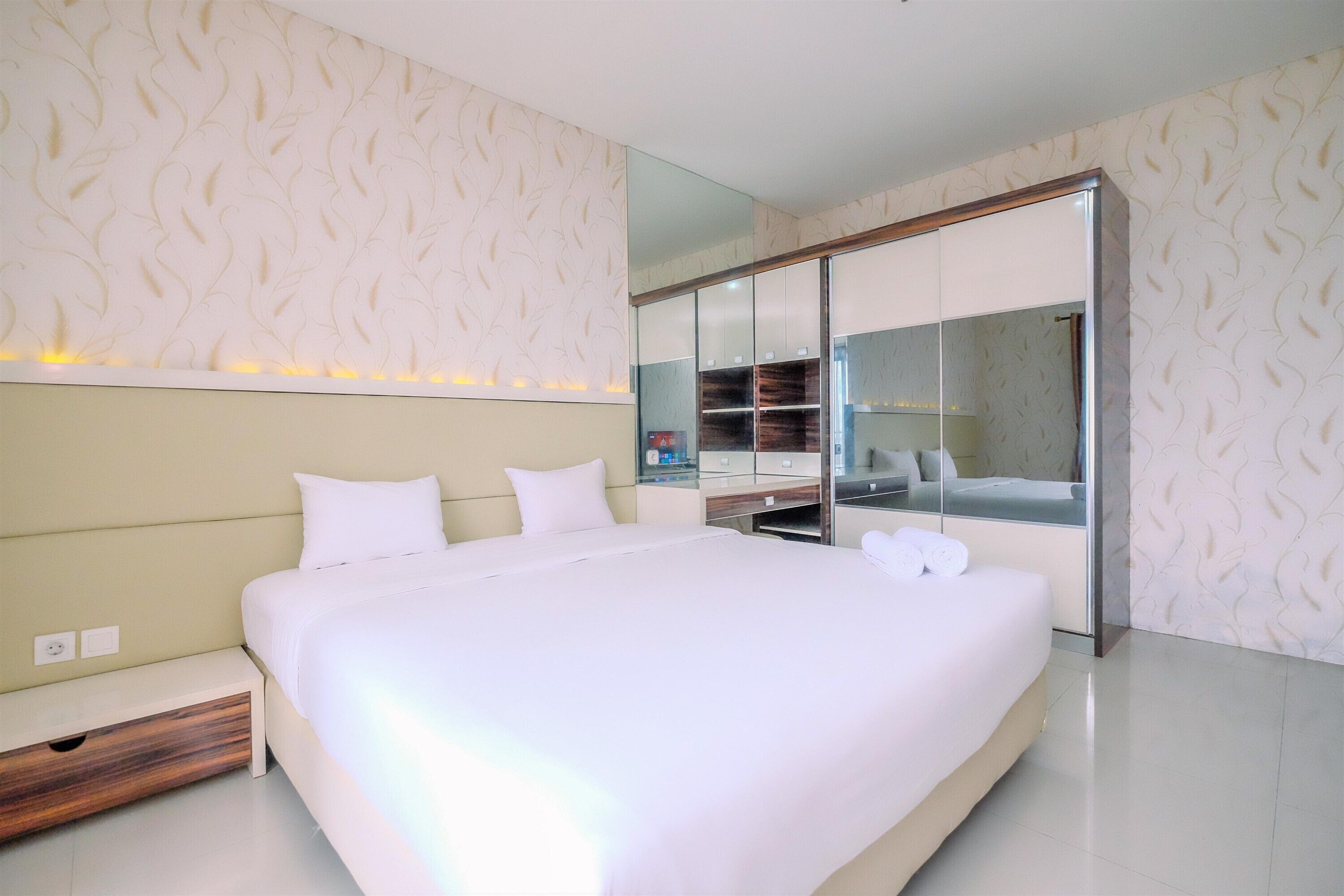 A modern hotel room with a large bed, a bedside table, a wardrobe, and a mirror.