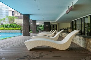 Área à beira da piscina com espreguiçadeiras, piscina e vista para a cidade.