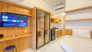A modern hotel room with a TV displaying streaming services, a wooden wardrobe, a built-in kitchen, and a neatly made bed. - Good Price And Homey Studio Tokyo Riverside Pik 2 Apartment (Teluknaga)