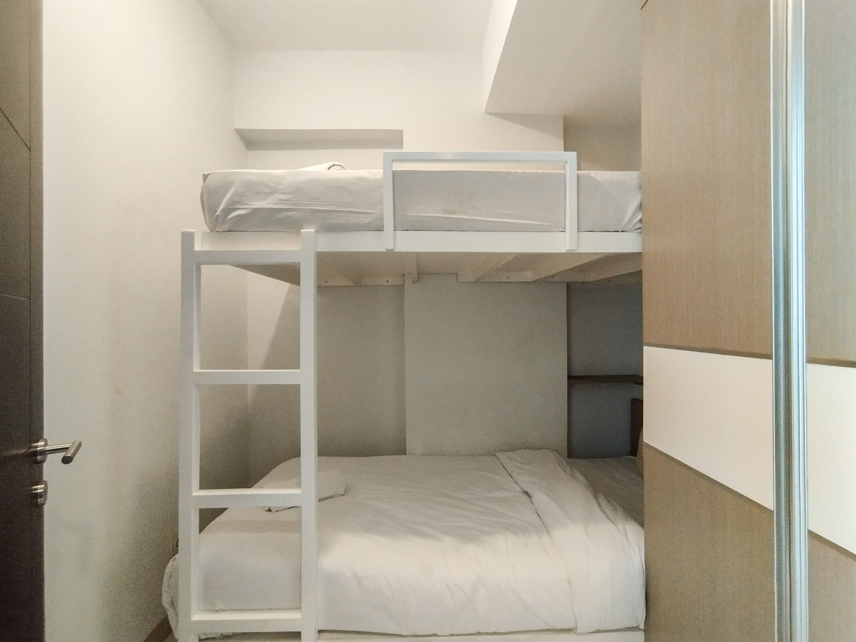 A bunk bed room with a ladder, white bedding, and a door.
