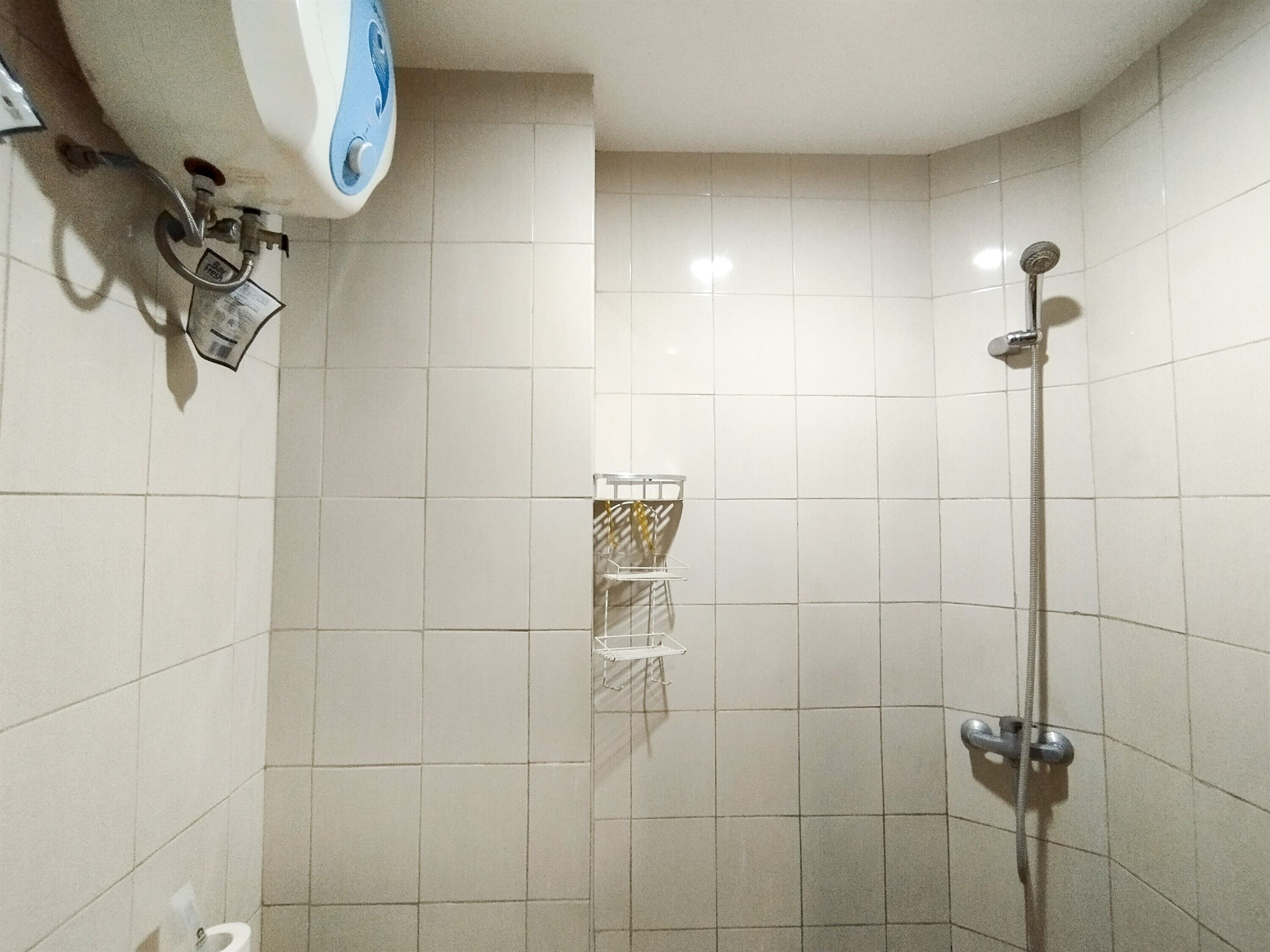 Une petite salle de bain carrelée, équipée d’une douche, d’un porte-serviettes et d’un distributeur de savon.