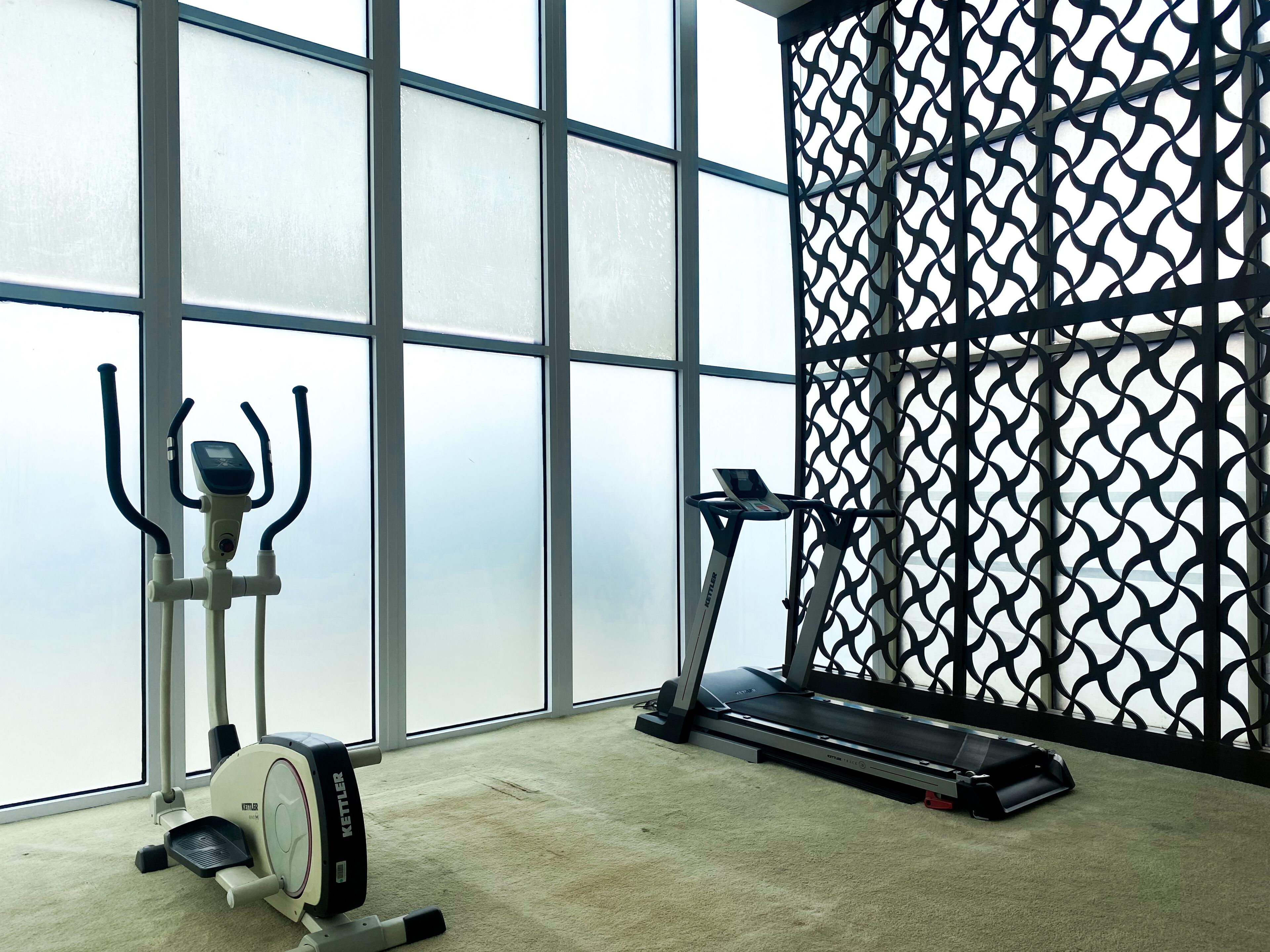 A gym with exercise equipment, large windows, and a patterned wall.