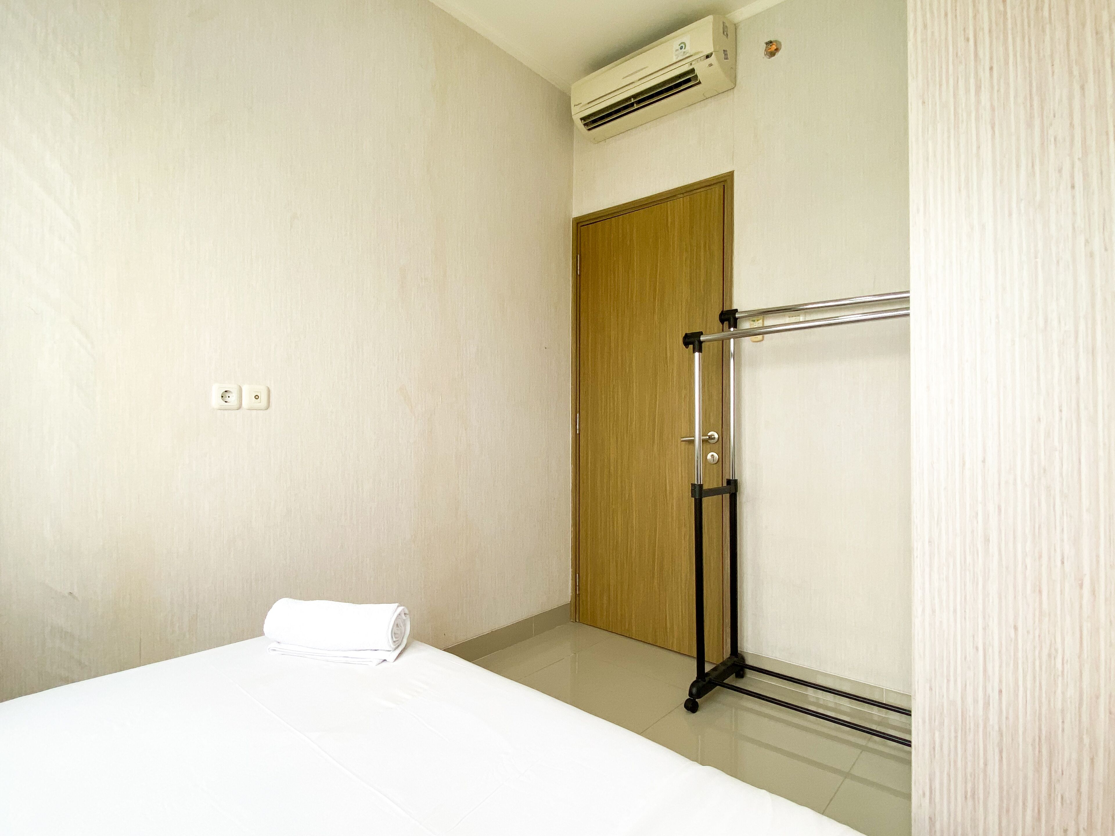 A hotel room with a bed, a wooden door, an air conditioning unit, and a towel on the bed.