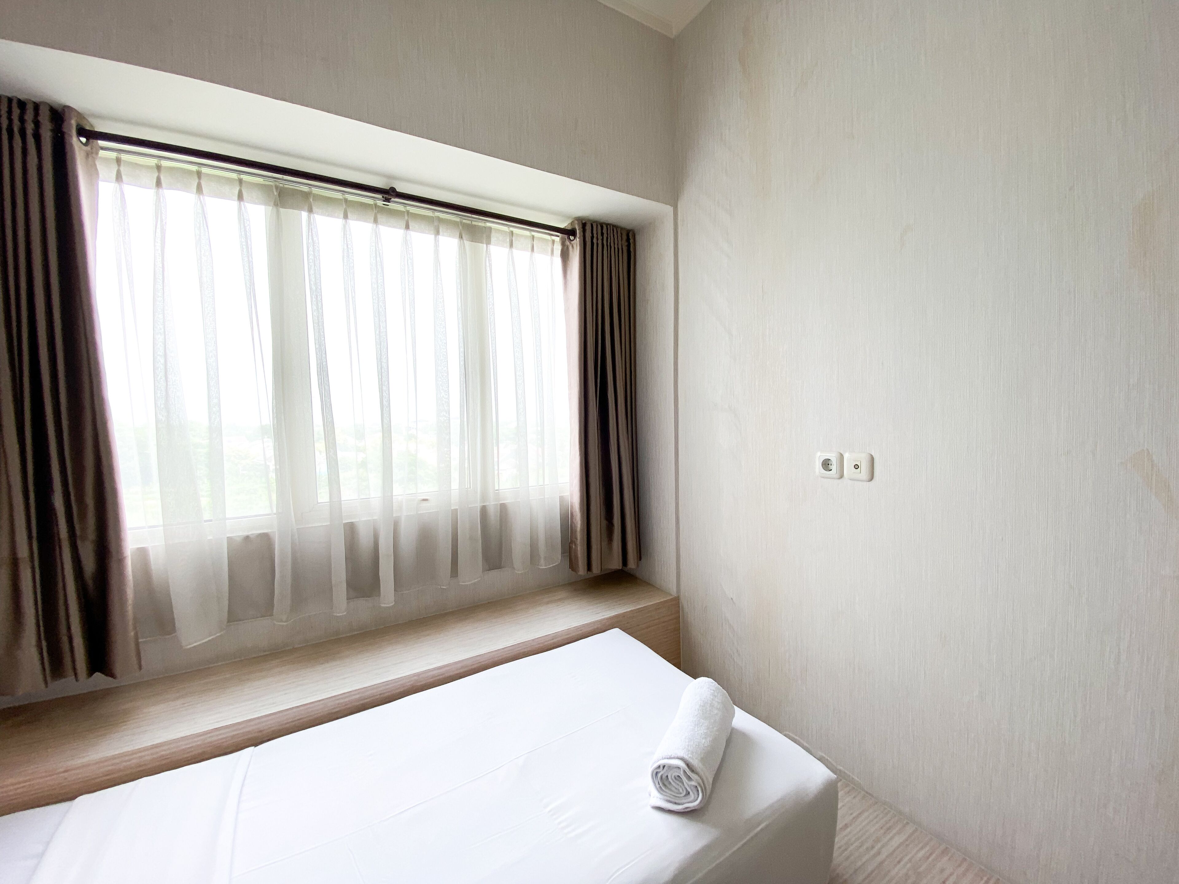 A hotel room with a bed, a window with sheer curtains, and a plain wall.