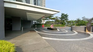 A modern building entrance with a curved pathway, a sculpture, and a sign indicating 'Amsterdam San Francisco'. - Well Designed And Strategic 2Br At Ciputra International Apartment (Jakarta)