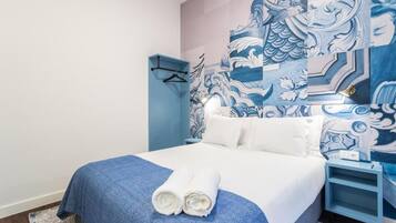 Une chambre d’hôtel avec un lit, un mur bleu orné d’un motif traditionnel, une table de chevet et une chaise bleue.