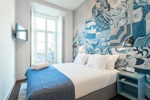 Una habitación de hotel moderna con una cama grande, un televisor de pantalla plana montado en la pared, una ventana con vistas y un mural decorativo.