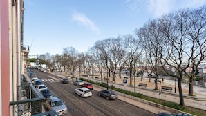 Vista de una calle con vías de tranvía, coches aparcados y una acera bordeada de árboles.
