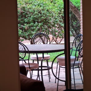 Een terras buiten met metalen tafels en stoelen, omgeven door groen.