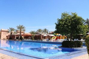 A swimming pool with a water slide, palm trees, and a building with a dome.