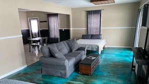 A room with a sofa, a bed, a small table, and a television.
