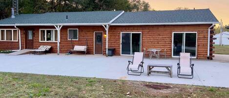 A log cabin with a patio area, including a table and chairs, and a swing set.