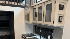 Een kleine keuken met een magnetron, een spoelbak en donkere kastjes.