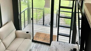 Een compact interieur met twee niveaus, een stapelbed op de bovenverdieping, een sofa op de benedenverdieping en een grote schuifdeur die leidt naar een terras.