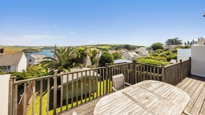 A wooden deck with a round table, a view of a lake, and surrounding houses. - Firm Anchor (Salcombe)