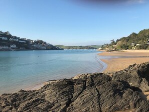 Una playa costera con primer plano rocoso, aguas tranquilas y edificios al fondo.