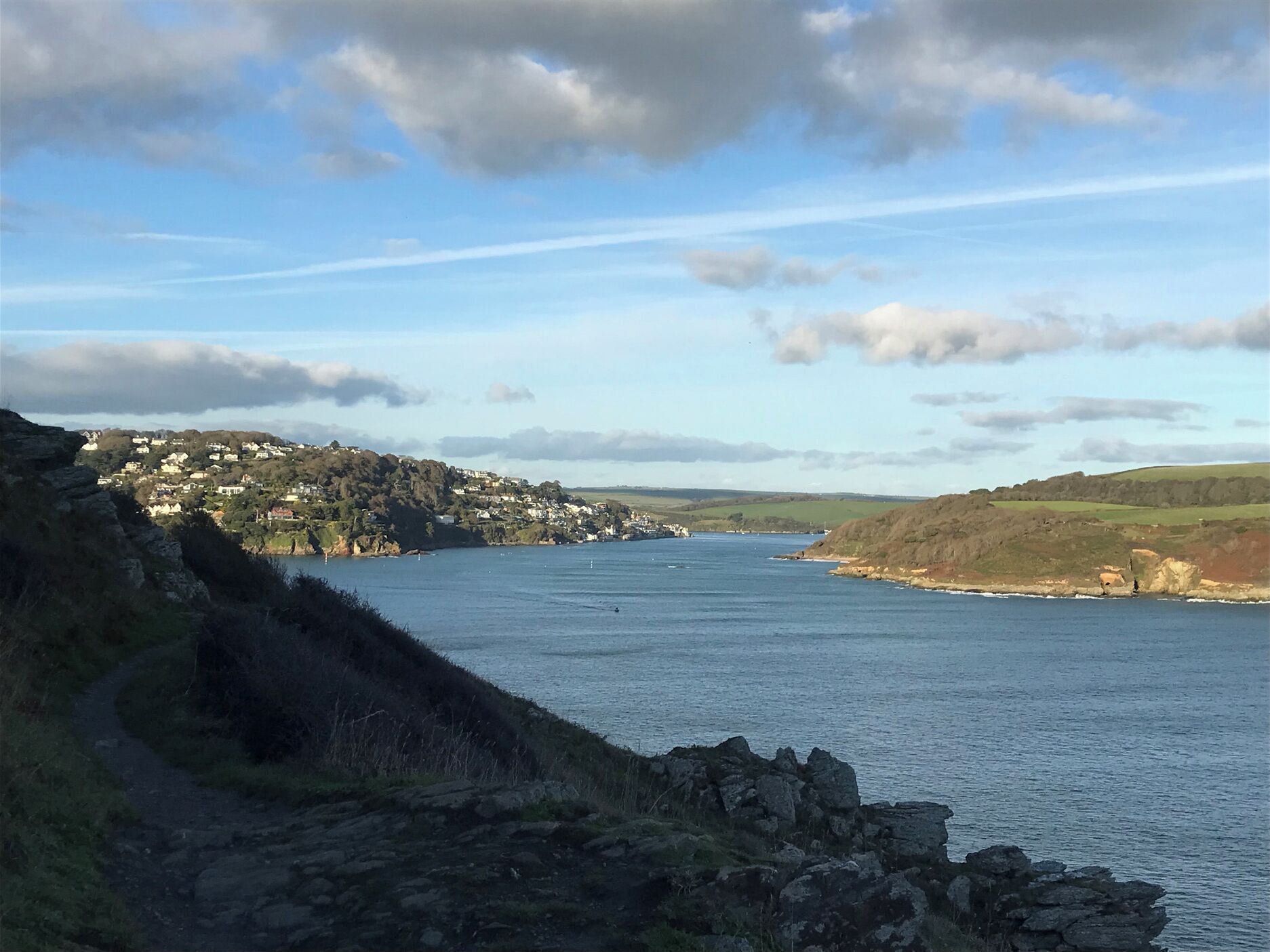 A coastal landscape with a clear view of a town on a hill, a body of water, and rocky terrain.
